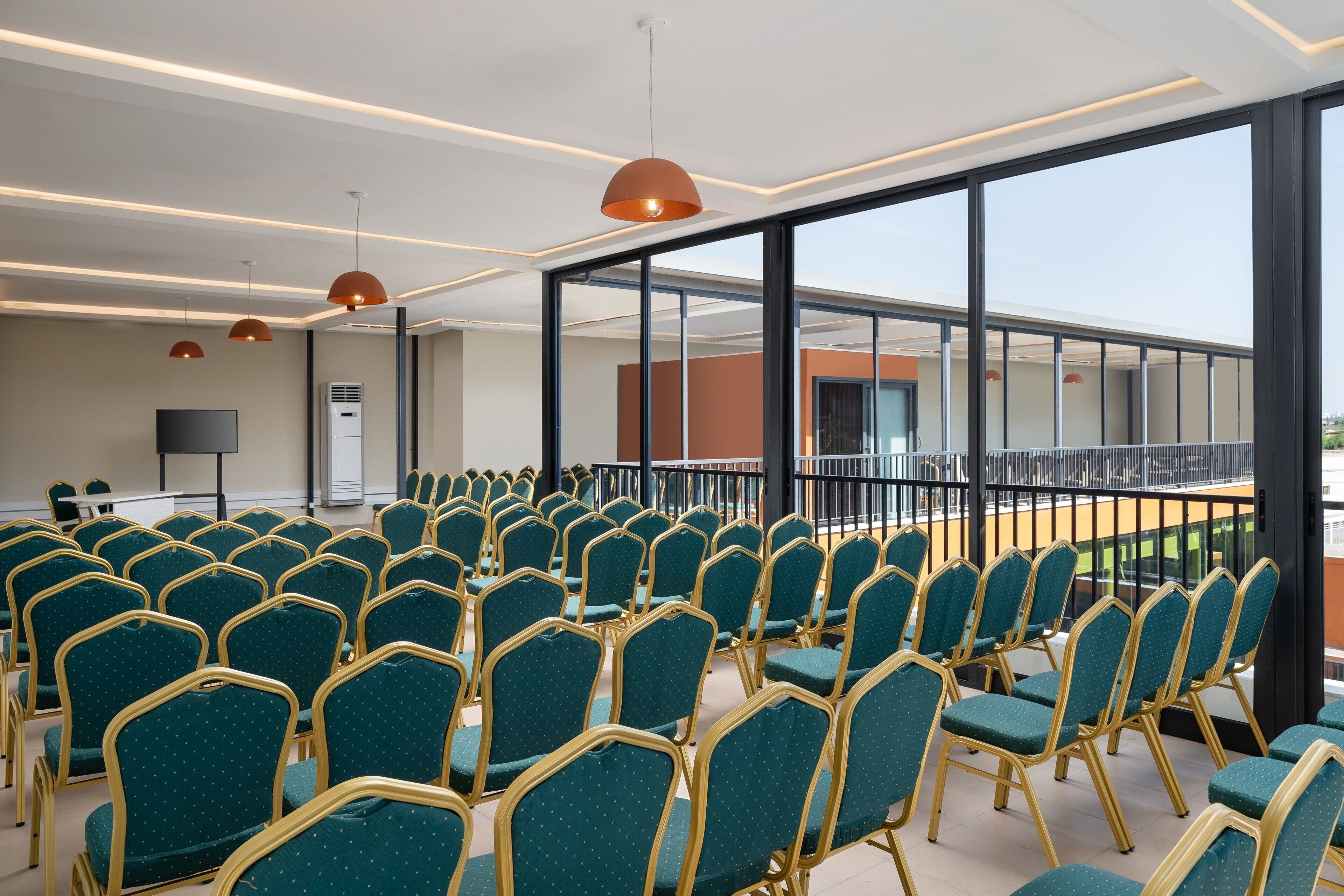 Una sala conferenze con file di sedie verdi, un'ampia finestra e un moderno design del soffitto.