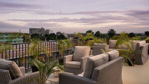 A rooftop terrace with wicker furniture and palm trees, overlooking a cityscape. - Protea Hotel Luanda (Luanda)