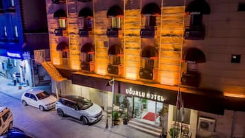 Un hôtel doté de nombreux balcons, avec une entrée bien visible et des voitures garées devant.