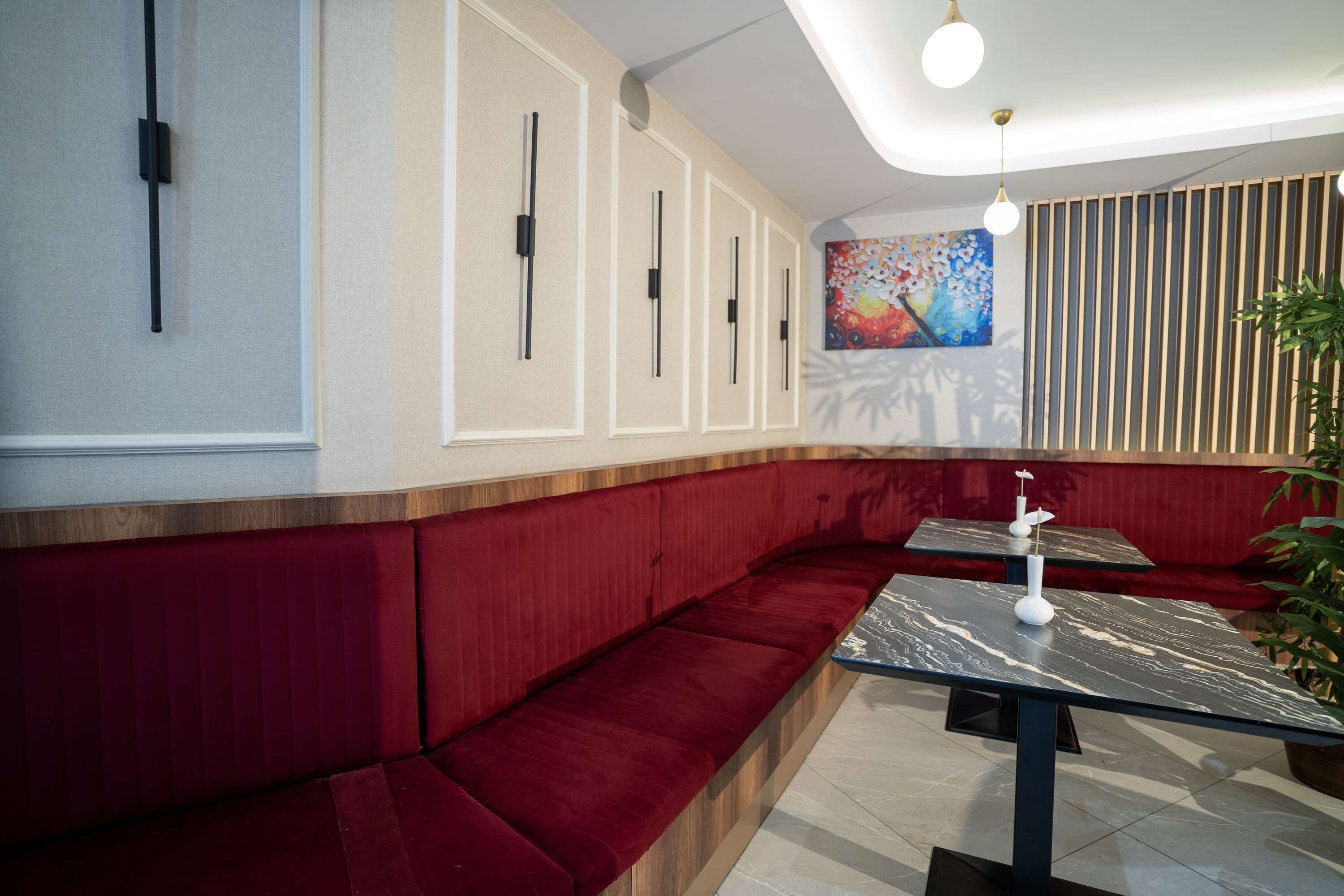 A restaurant with red cushioned seating, a marble table, and a colorful painting on the wall.
