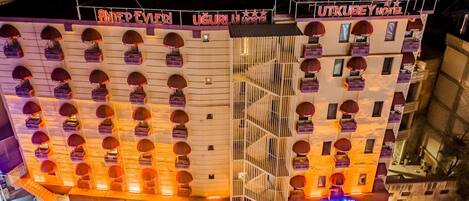 Un hotel con varios balcones, una escalera central y un letrero que dice 'UTKUBEY HOTEL'.