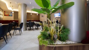 A modern lobby with a large plant centerpiece, seating area, and a television mounted on the wall. - Uğurlu Hotel (Gaziantep)