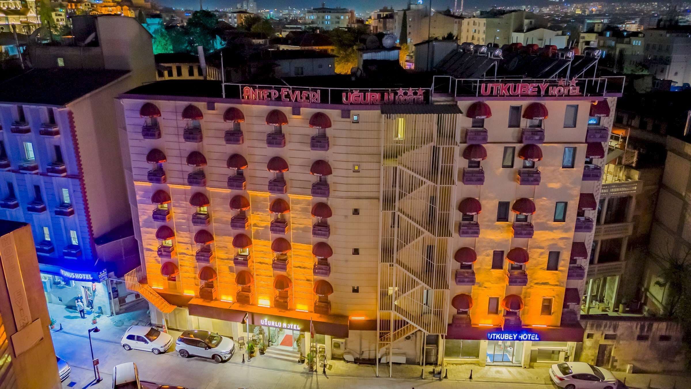 A multi-story hotel with a row of rooms on each floor, a visible entrance, and a parking area with cars.