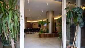 A hotel lobby with a red carpet, potted plants, a wooden reception desk, and a large pillar. - Uğurlu Hotel (Gaziantep)