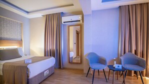A hotel room with a bed, two checkered chairs, a small table, an air conditioning unit, and a mirror. - Uğurlu Hotel (Gaziantep)
