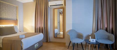 Une chambre d’hôtel comprenant un lit, deux chaises, une petite table, un appareil de climatisation et un miroir.