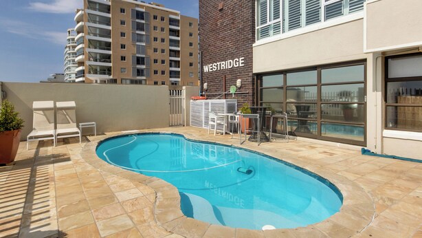 A swimming pool area with lounge chairs, a brick building labeled "WESTRIDGE", and a view of other residential buildings.