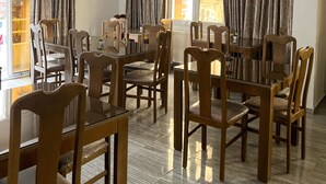 A dining area with wooden chairs and tables, large windows with curtains, and an air conditioning unit on the wall. - Hôtel Métropole Résidence  (Tunis)