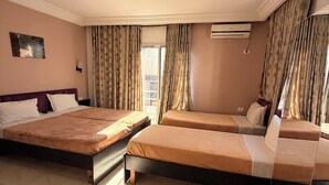 A hotel room with two beds, a window with curtains, an air conditioning unit, and a wall-mounted light. - Hôtel Métropole Résidence  (Tunis)