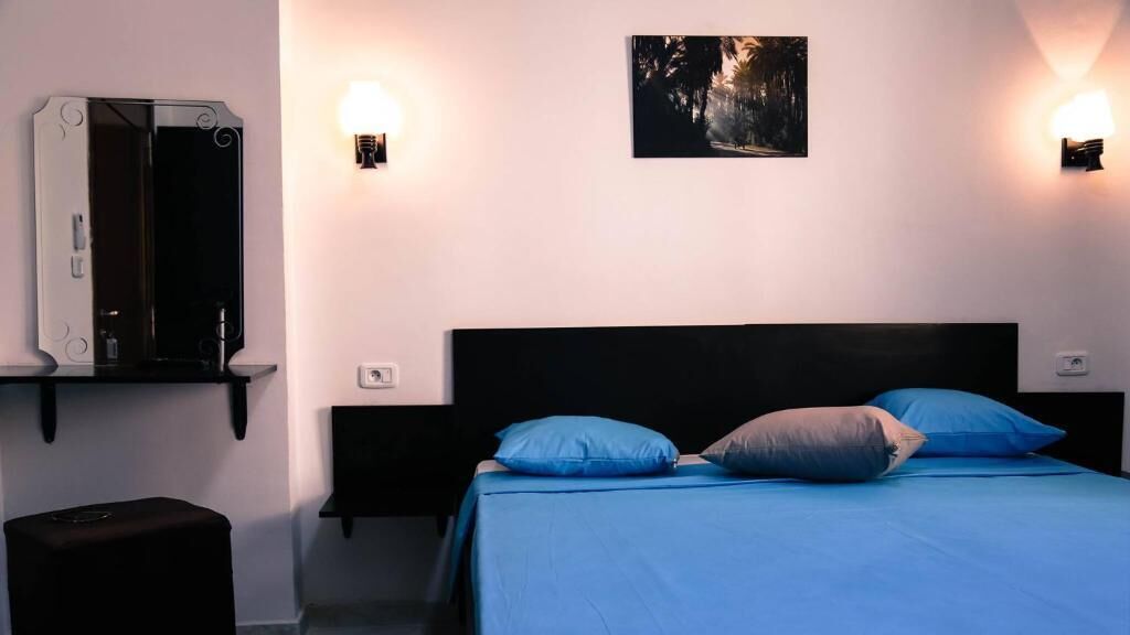 A bedroom with a bed, two wall-mounted light fixtures, a black headboard, and a framed picture on the wall.
