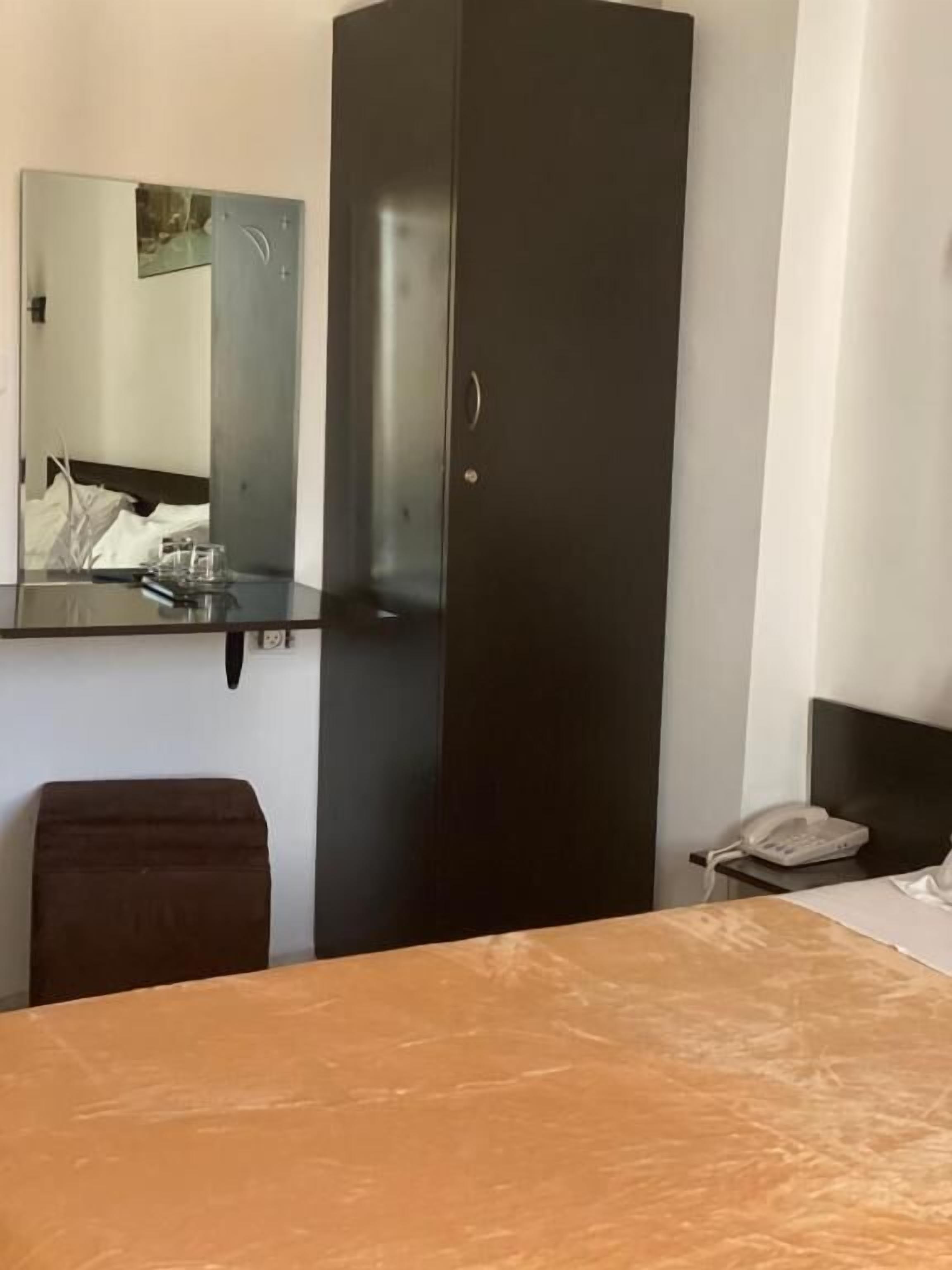 Ein Hotelzimmer mit Bett, Schreibtisch, Stuhl, Kleiderschrank, Spiegel und Nachttischtelefon.