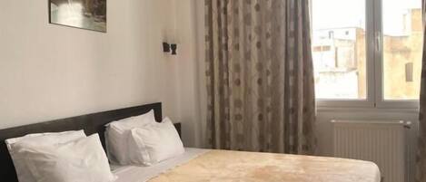 A bedroom with a large bed, a headboard, a window with curtains, and a painting on the wall.