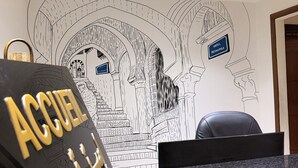 A reception desk with a black and gold sign reading "ACCUEIL" and a wall mural depicting a hotel interior with a sign reading "HOTEL METROPOLI". - Hôtel Métropole Résidence  (Tunis)