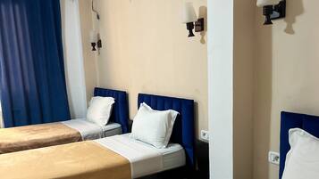 A hotel room with two beds, a blue headboard, white bedding, an air conditioning unit, and wall-mounted lamps.