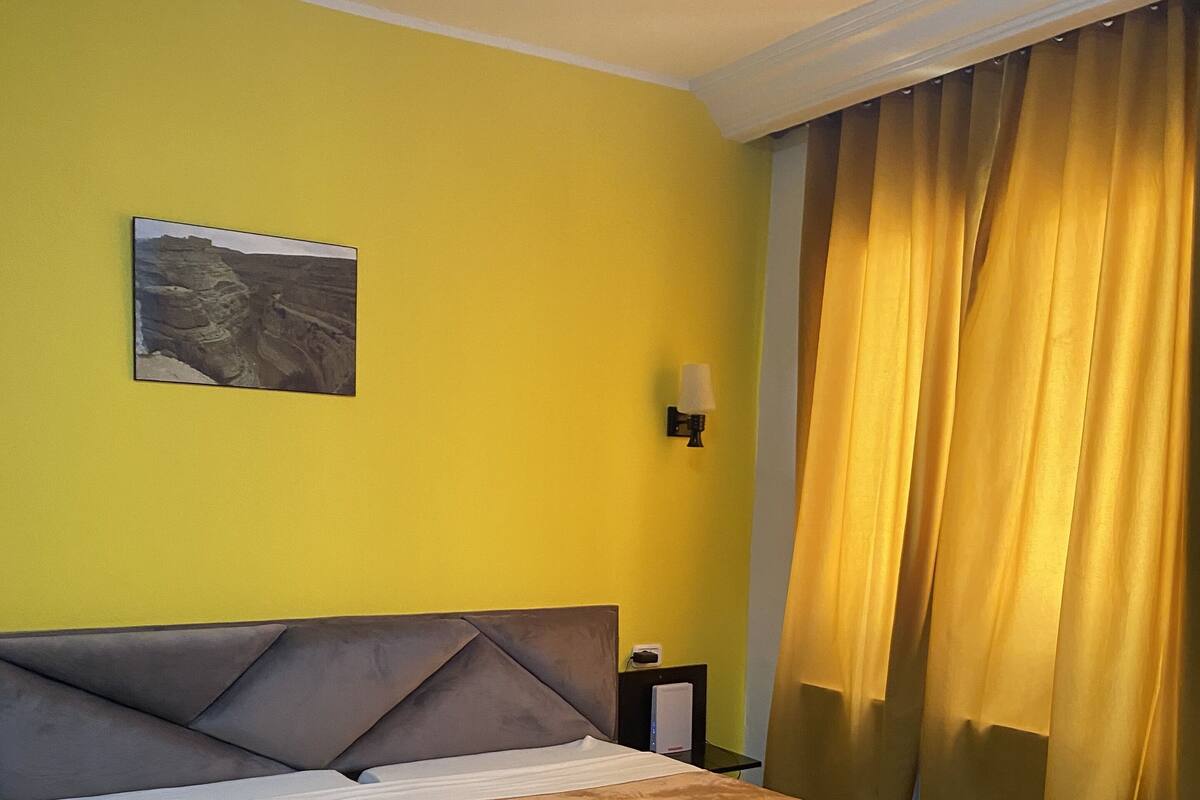 A bed with a brown cover, a headboard, and a wall-mounted lamp.