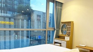 A hotel room with a large bed, a wooden desk, a mirror, and a window overlooking a building with a sign reading "CENTURYON LUXURY GYM BY CALIFORNIA".