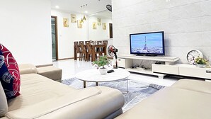 A modern living room with a flat-screen TV, a dining area with chairs, and a sofa with a patterned cushion.