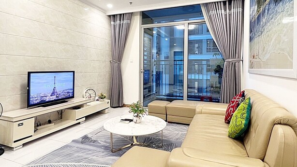 A modern living room with a sofa, a coffee table, a TV, and a balcony with curtains.