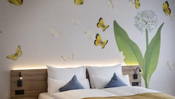 Quarto com cama, almofadas, mesa de cabeceira, luminária na parede e adesivos de borboletas.