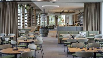 Restaurante moderno com mesas redondas e cadeiras verdes, área de bar e um espaço de estar com sofá e cadeiras.