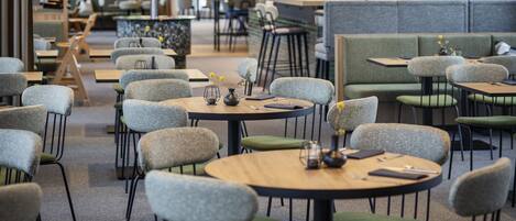 Un interior de restaurante moderno con mesas redondas, sillas acolchadas y una zona de bar.