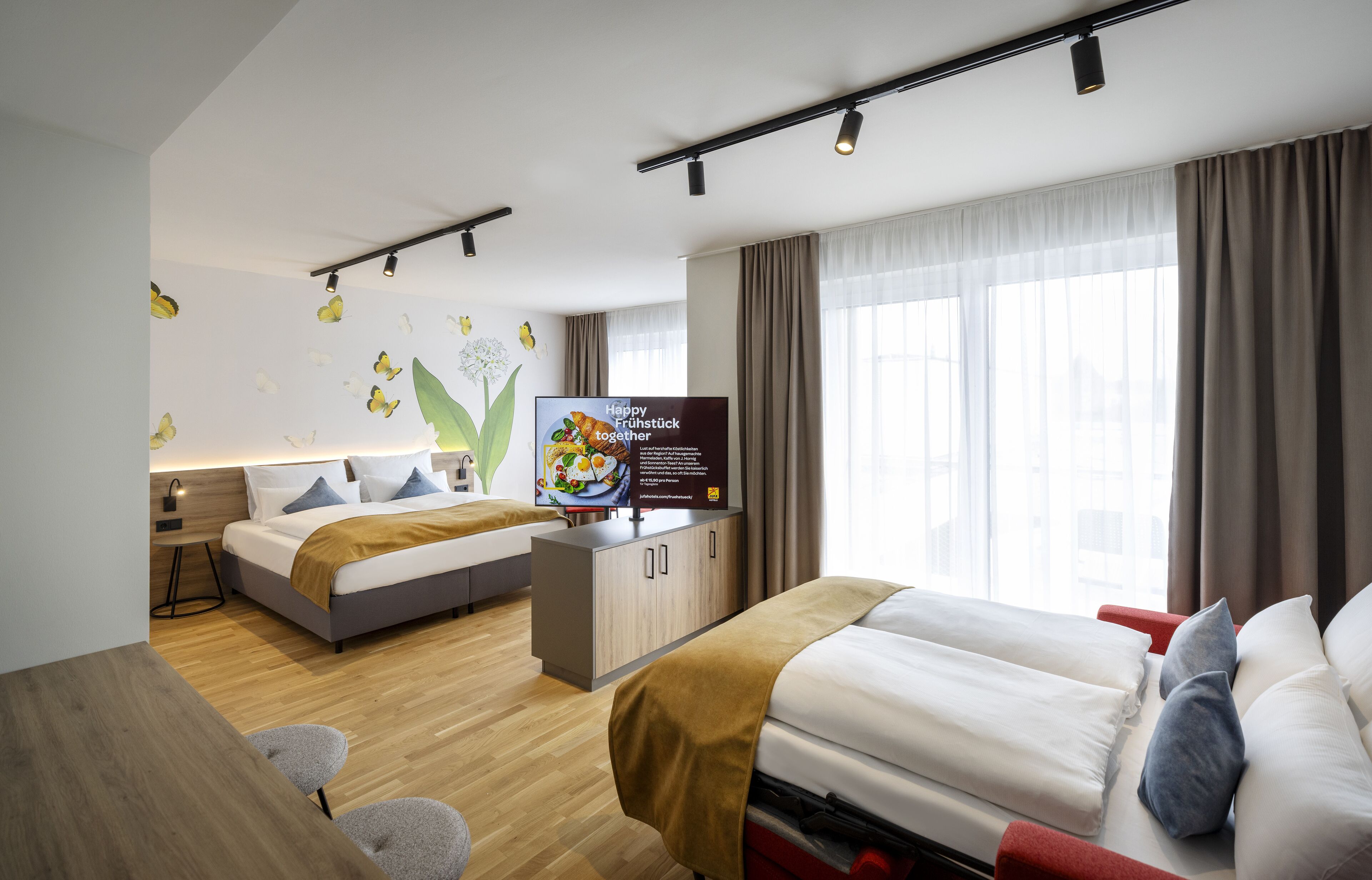 Ein modernes Hotelzimmer mit Bett, Schreibtisch, Fernseher und einem großen Fenster.