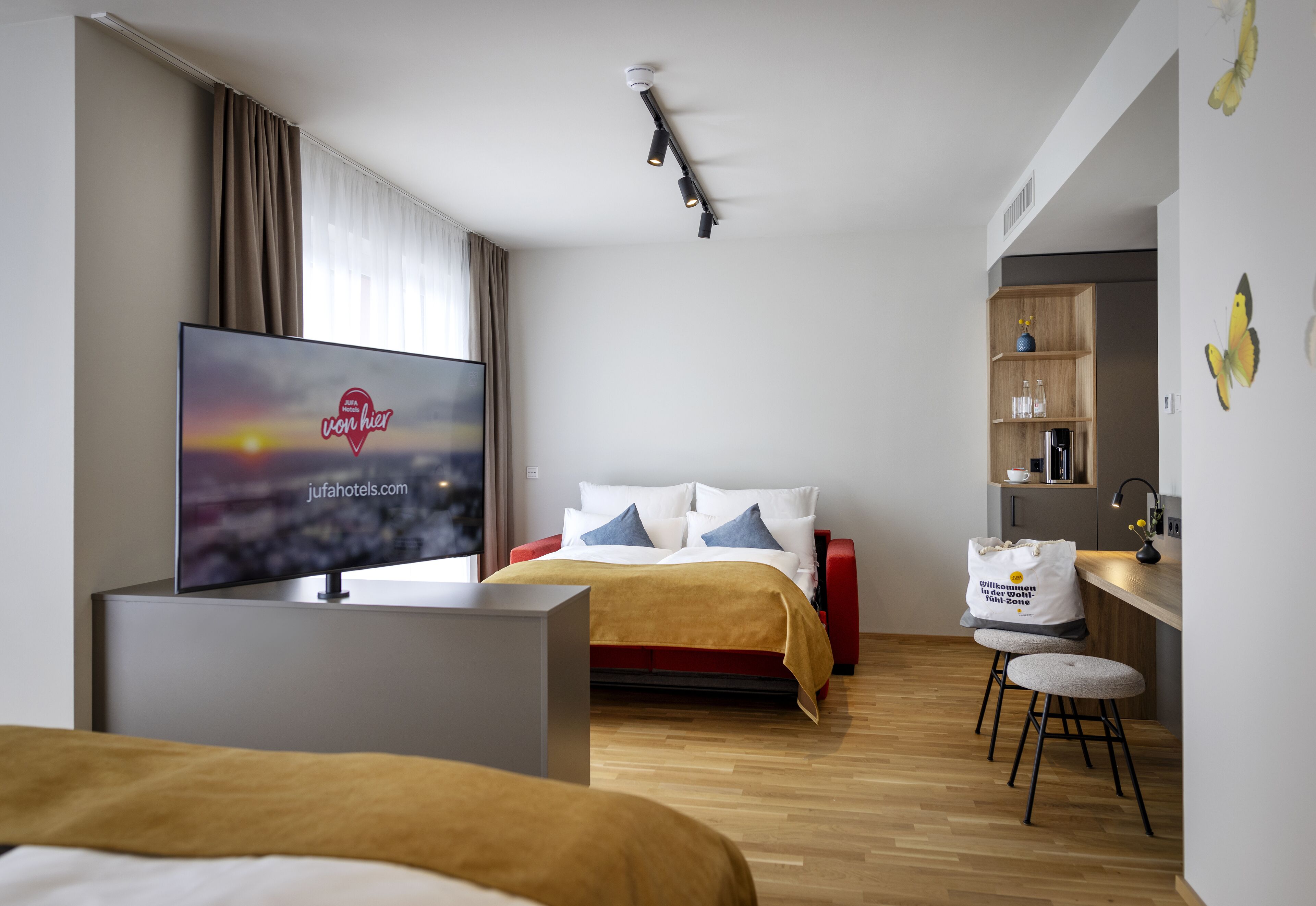 Una habitación de hotel moderna con una cama, televisor, escritorio y kitchenette.