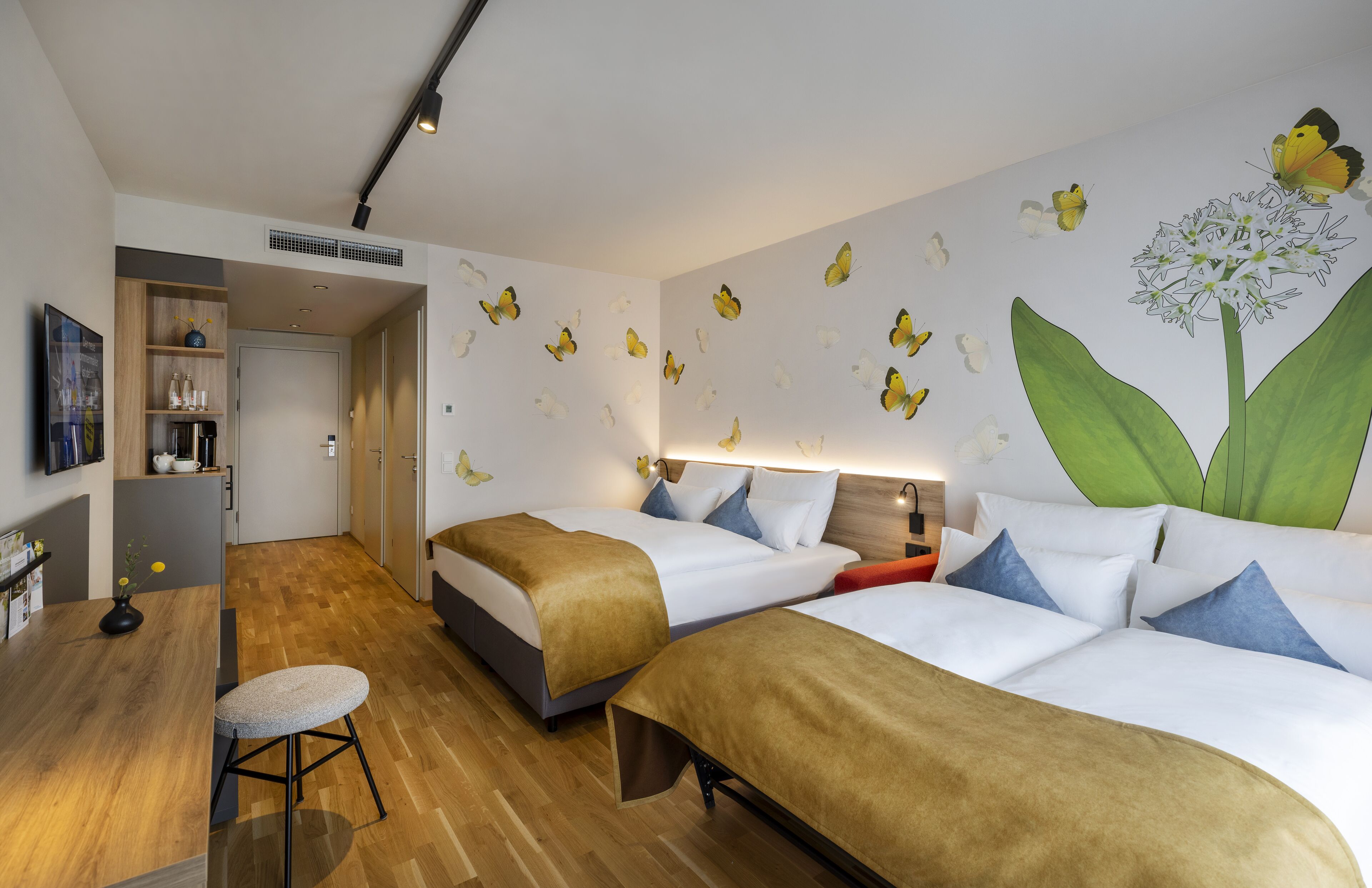 A hotel room with two beds, a small table, a stool, and a wall decorated with butterfly decals.