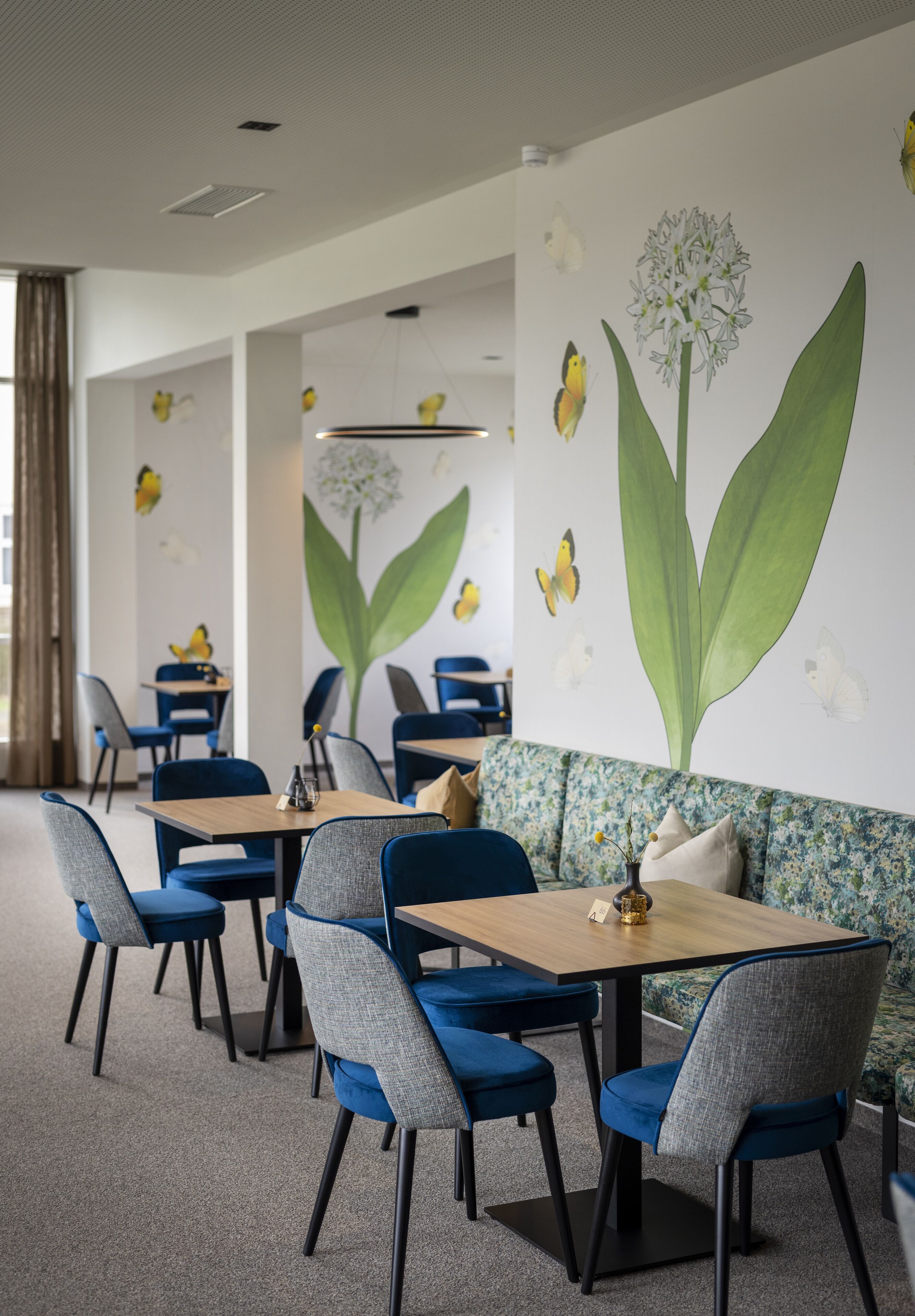 Un comedor moderno con sillas azules, mesas de madera y un mural floral en la pared.