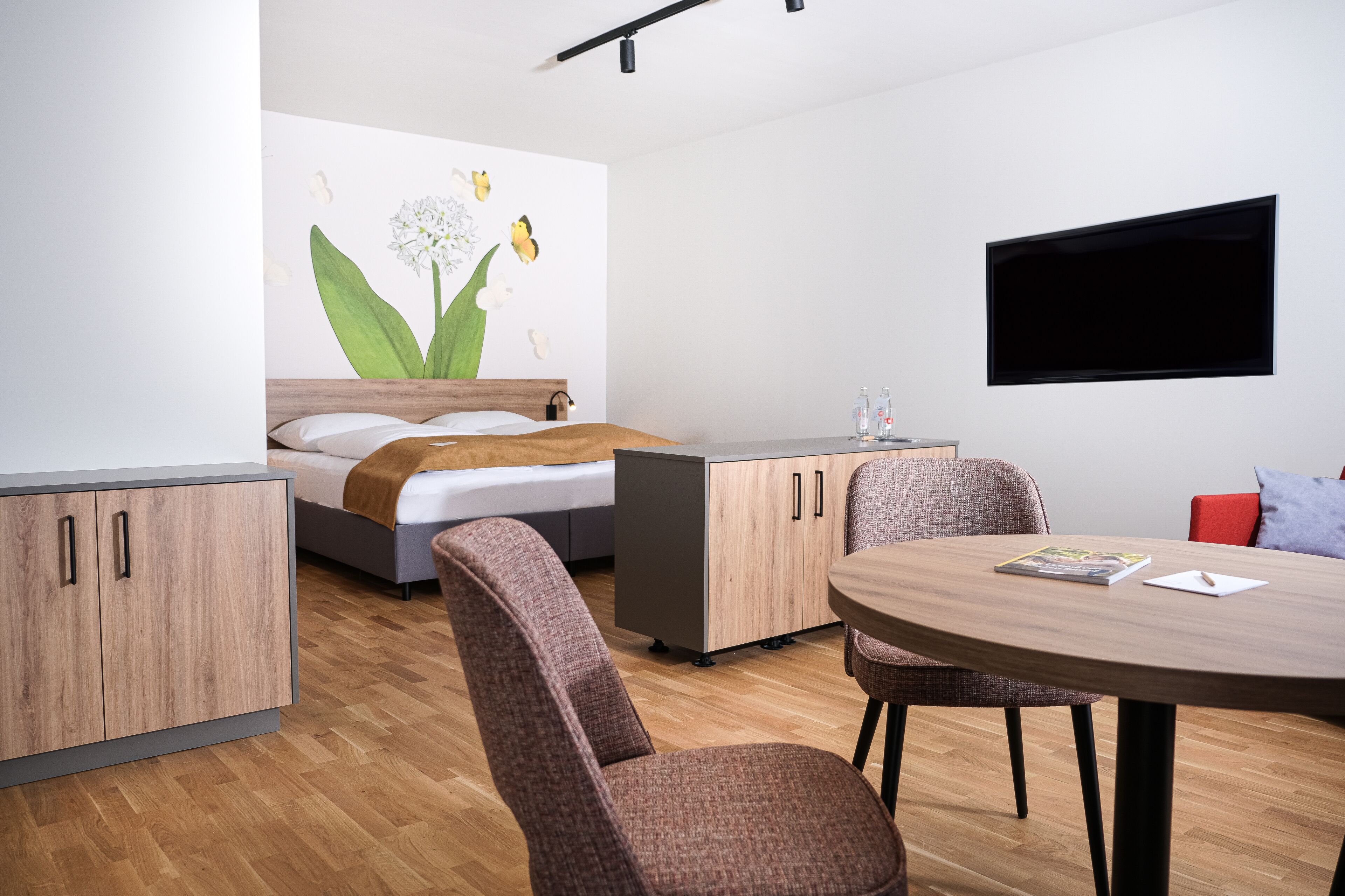 A modern room with a bed, a desk, a chair, a round table, and a TV mounted on the wall.