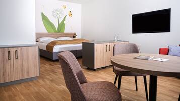 A modern room with a bed, a desk, a chair, a round table, and a TV mounted on the wall.