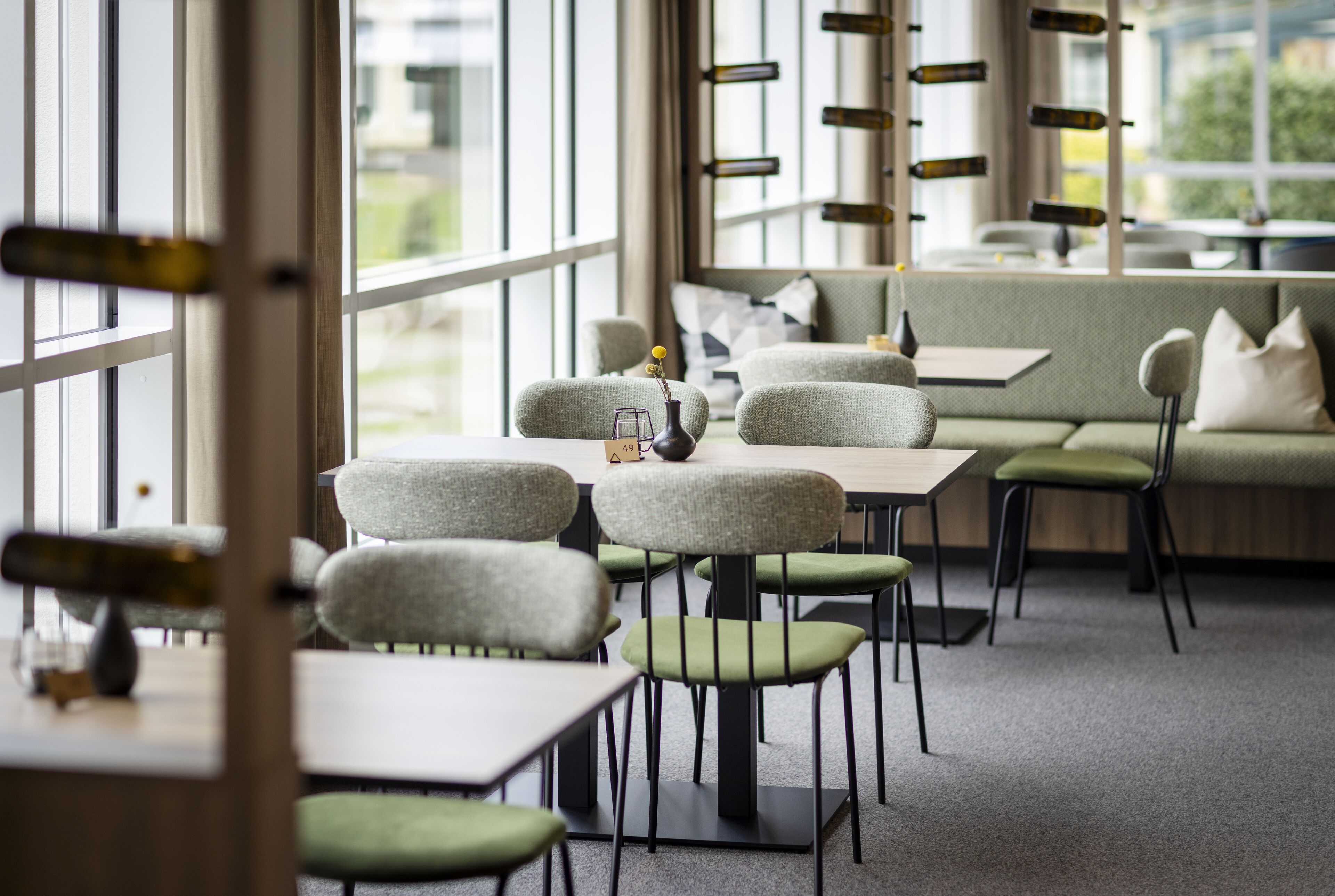 Een moderne eetruimte met hoge tafels en stoelen, een bank en grote ramen.
