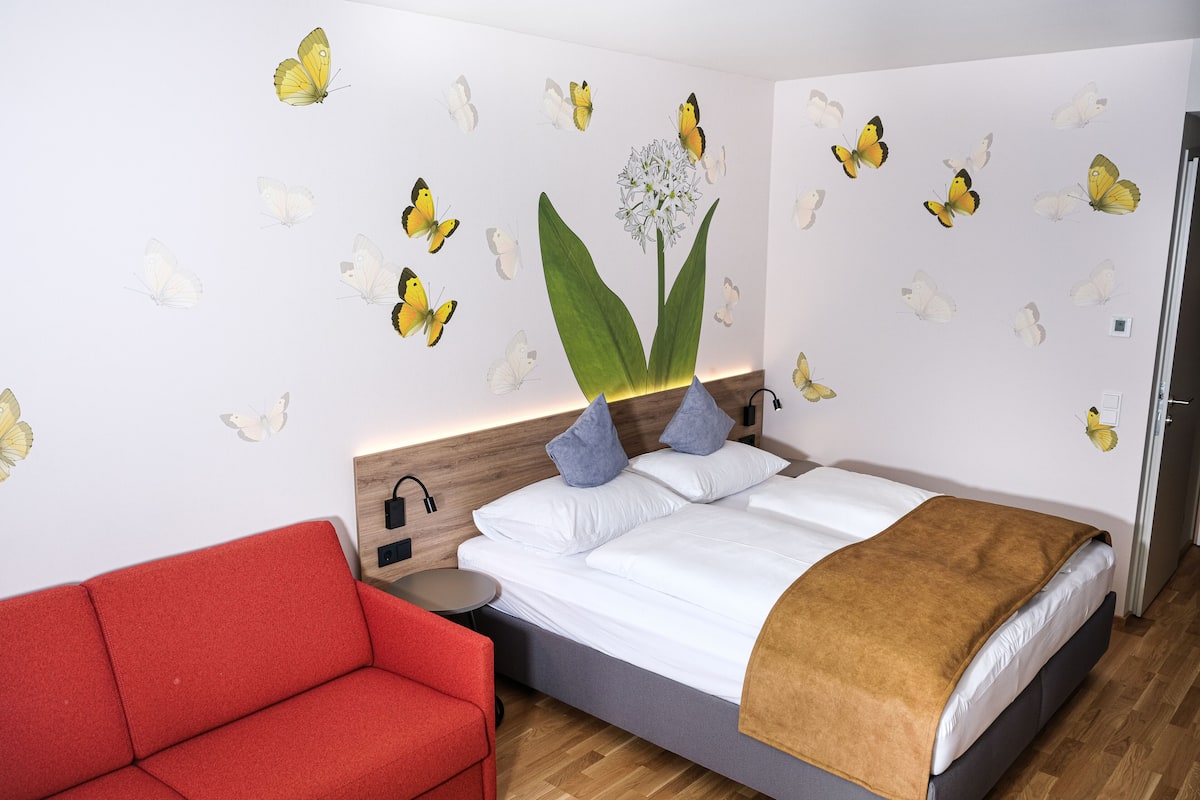 Ein Schlafzimmer mit einem Bett, einem roten Sofa und Wanddekorationen mit Schmetterlingen.