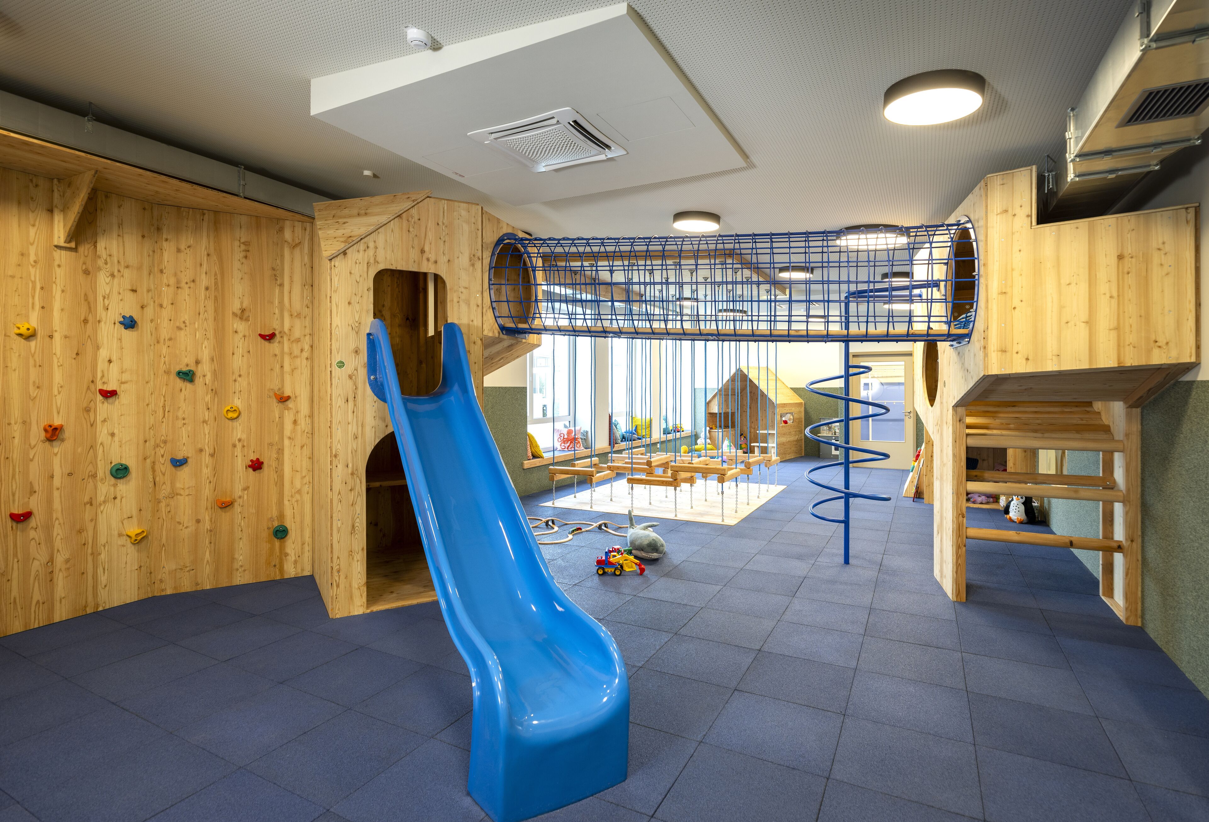 A children's play area with a blue slide, climbing wall, and wooden play structures.