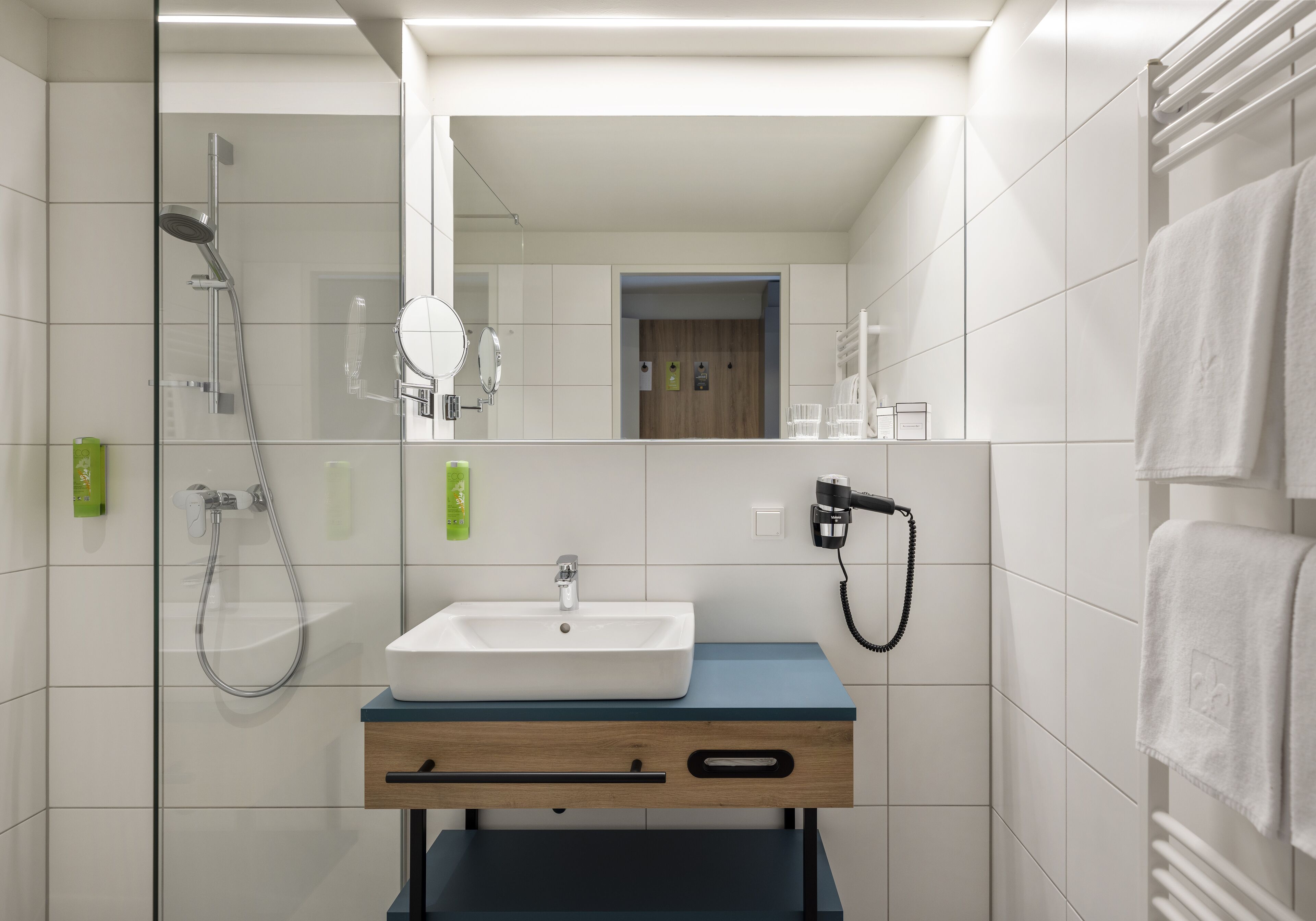 A modern bathroom with a white sink, a mirror, a shower, and a towel rack.