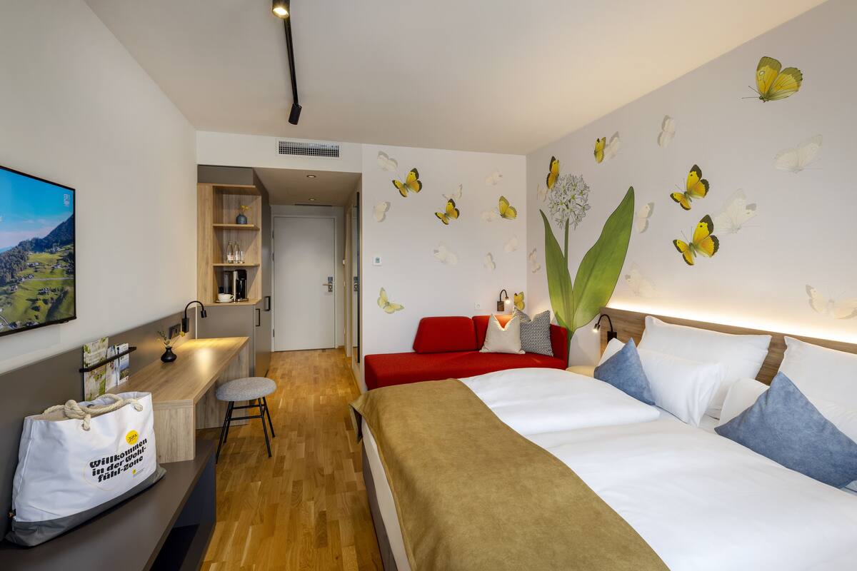 Ein Hotelzimmer mit einem Bett, einem roten Sofa, einem Holztisch und einer Wand mit Schmetterlingsstickern.