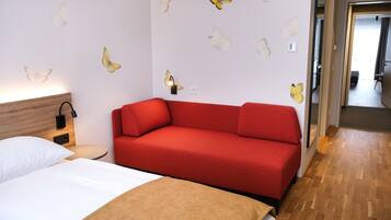 Habitación de hotel con sofá rojo, cabecera de madera, cama blanca y adhesivos de pared con mariposas.