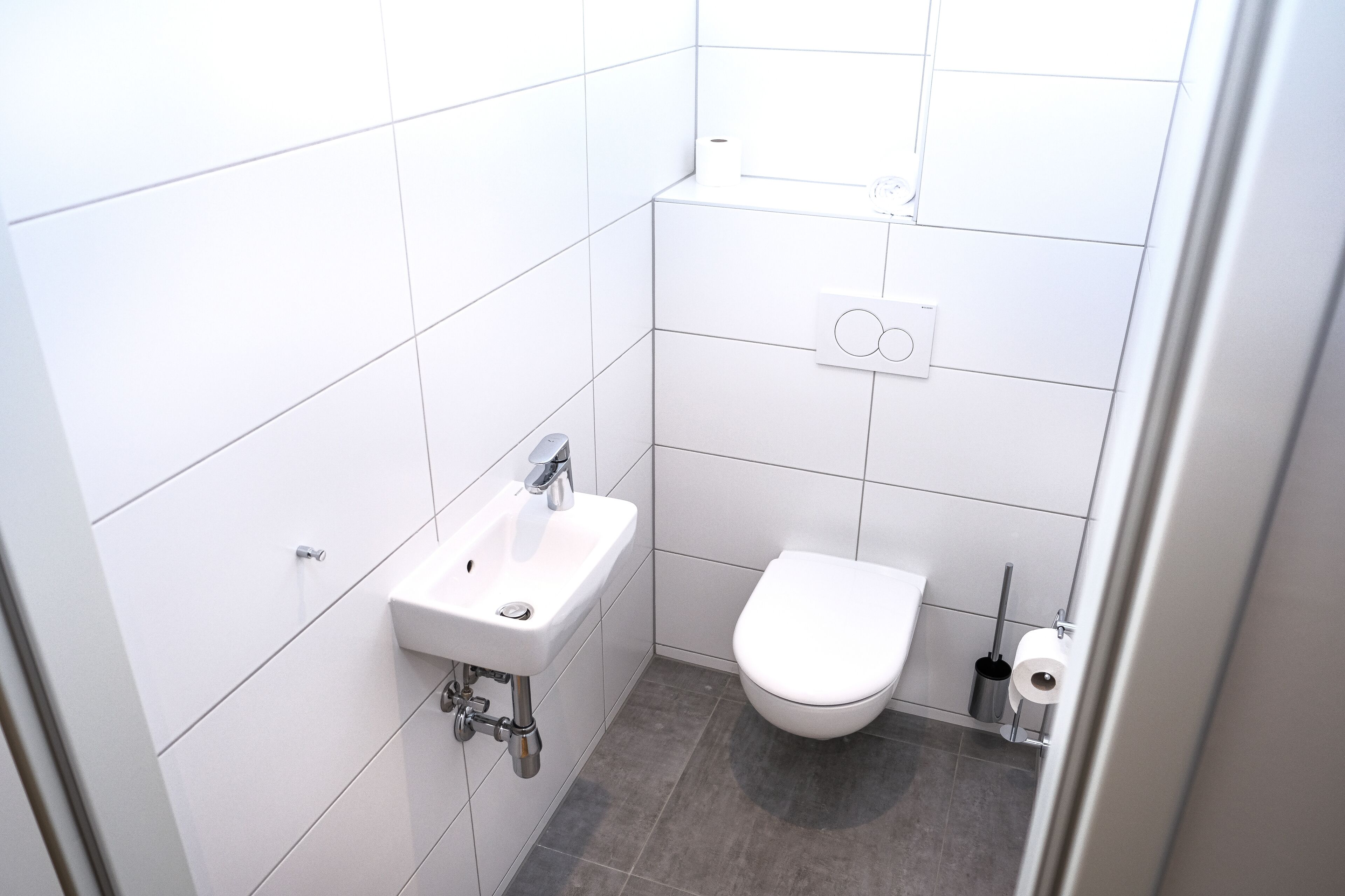 Un baño pequeño y moderno con azulejos blancos, un lavabo blanco y un inodoro.
