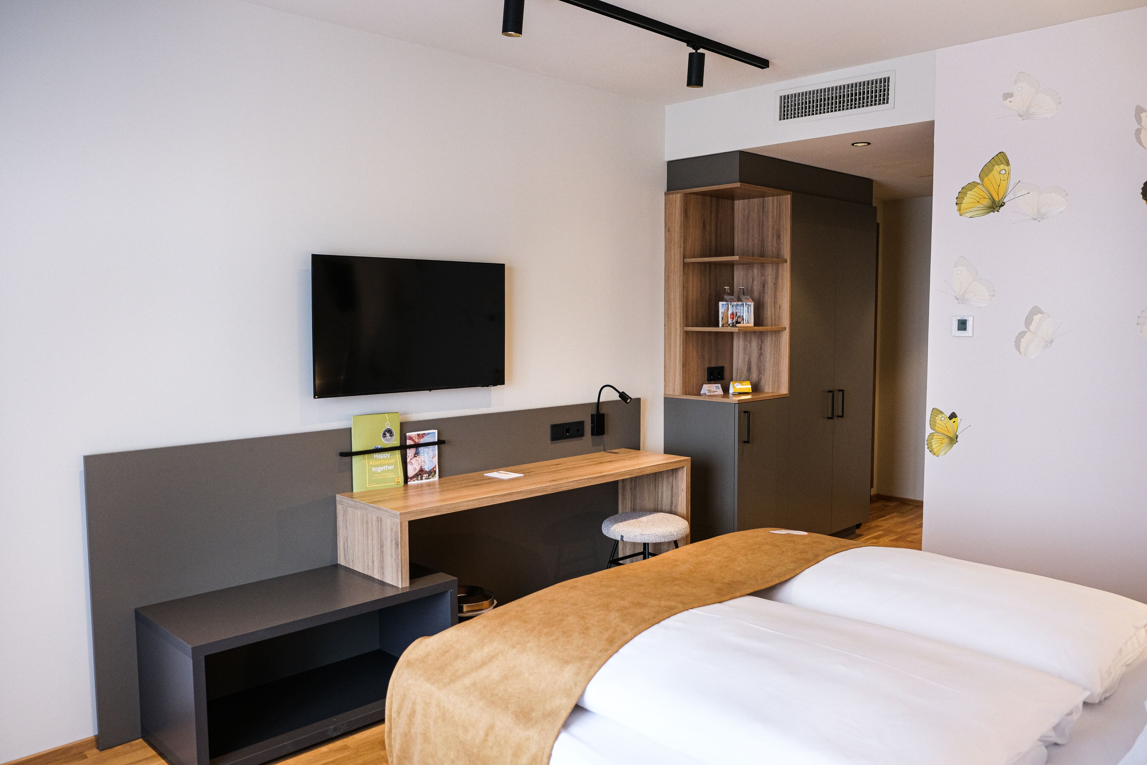 Una habitación de hotel moderna con una cama, un escritorio, un televisor y un armario.