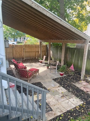 A covered patio area with outdoor furniture, a wooden pergola, and a fenced backyard.