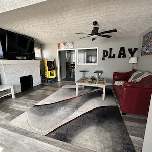 A living room with a fireplace, a TV, a gaming console, a red couch, and a 'PLAY' sign on the wall.