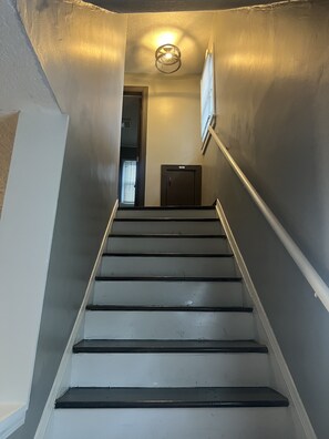 A staircase with a handrail, a door at the top, and a light fixture on the wall.