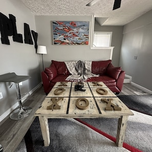 A living room with a red leather couch, a coffee table with wooden letter blocks spelling "XOXO", a lamp, and a painting on the wall.
