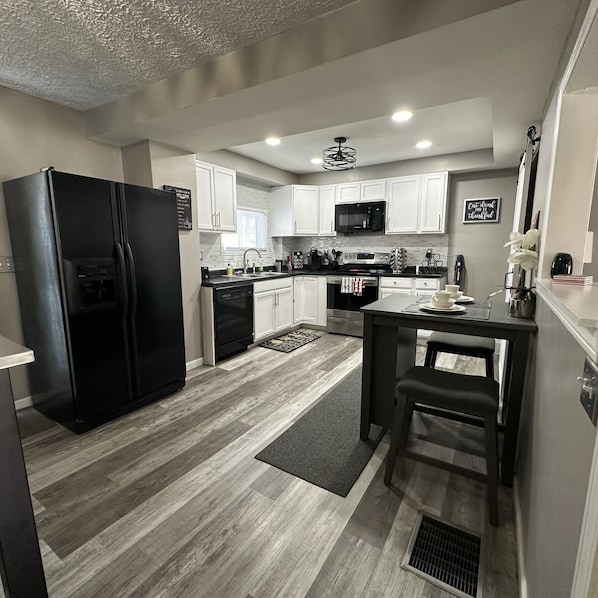 A modern kitchen with a black refrigerator, white cabinets, a microwave, and a dining area with a table and chair.