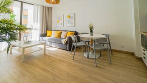 Ein modernes Wohnzimmer mit Sofa, Couchtisch, Esstisch und Stühlen. Eine Pflanze, Kunstwerke an der Wand und ein Blick durch das Fenster sind zu sehen.