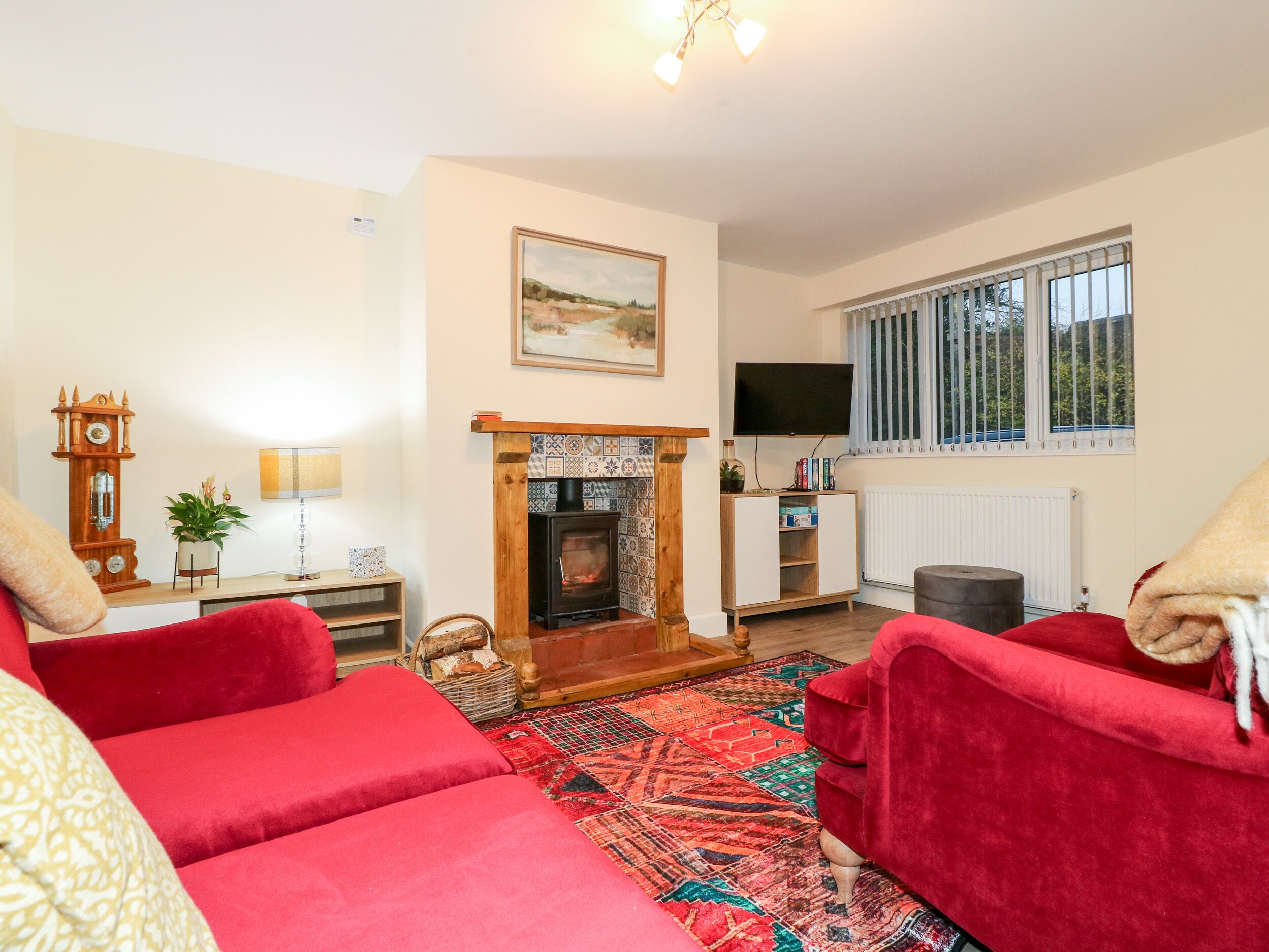 A cozy living room with red sofas, a fireplace, a clock, and a television.