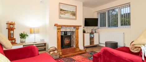 A cozy living room with red sofas, a fireplace, a clock, and a television.