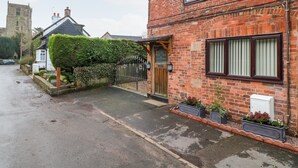 A brick house with a wooden front door, a small garden with potted plants, and a paved driveway. - 8 Church Lane (Stoke-on-Trent)