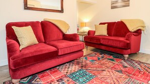 A living room with two red sofas, a patterned rug, a framed mirror, and a painting on the wall. - 8 Church Lane (Stoke-on-Trent)