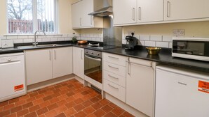 A kitchen with white cabinets, a black countertop, a stainless steel range hood, a coffee maker, and a microwave. - 8 Church Lane (Stoke-on-Trent)